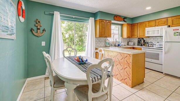 A kitchen with a dining area, wooden cabinets, a white refrigerator, and a window with curtains. - 2-home Nature Coast Retreat Near 3 Sisters Springs (Homosassa)