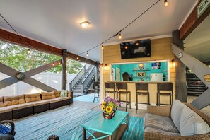 Ein überdachter Außenbereich mit einer Sitzecke, einem Tisch mit Blumenvase und einer Bar mit Sesseln und einem Fernseher.
