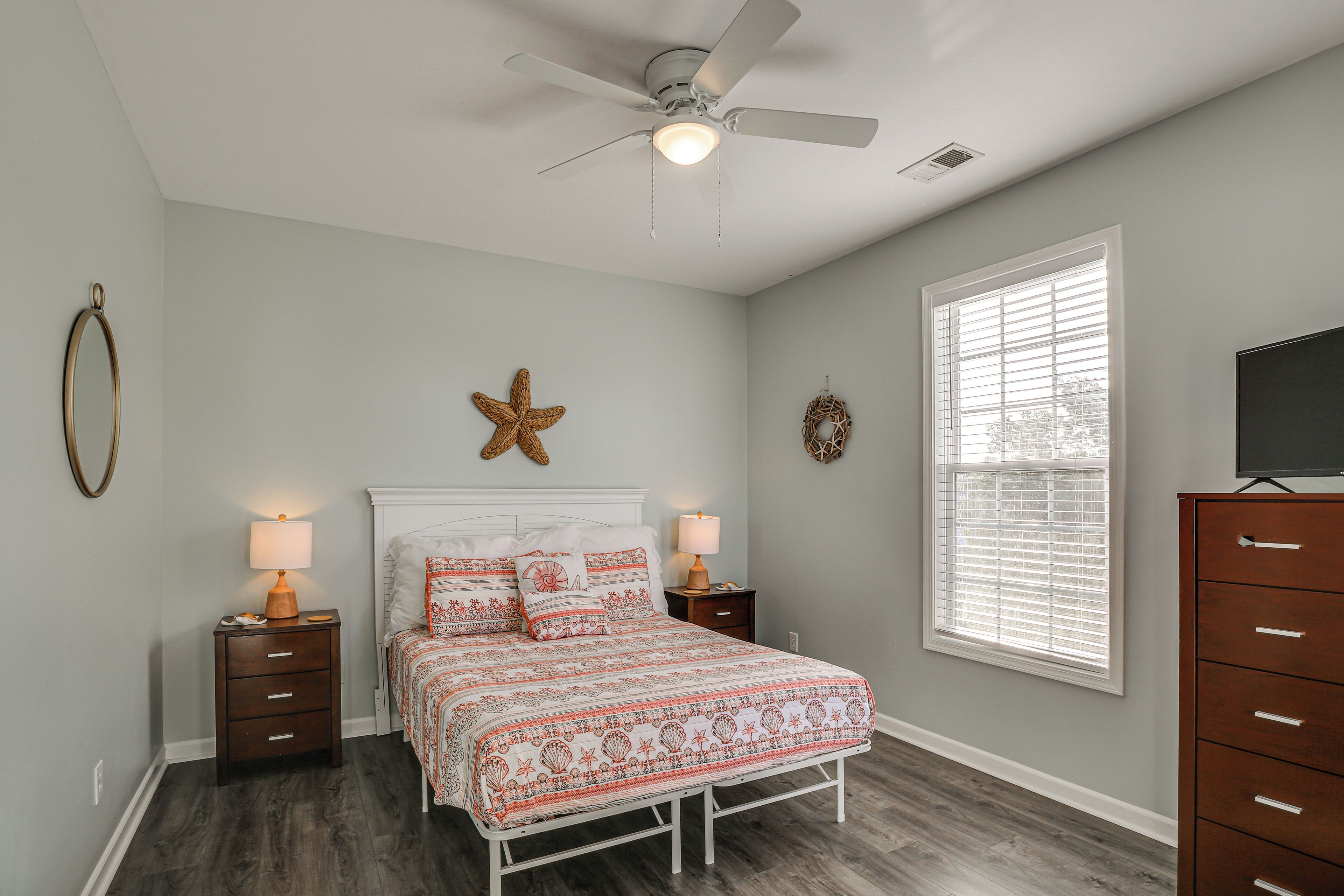 A bedroom with a bed, two nightstands, a ceiling fan, a window with blinds, and a dresser.