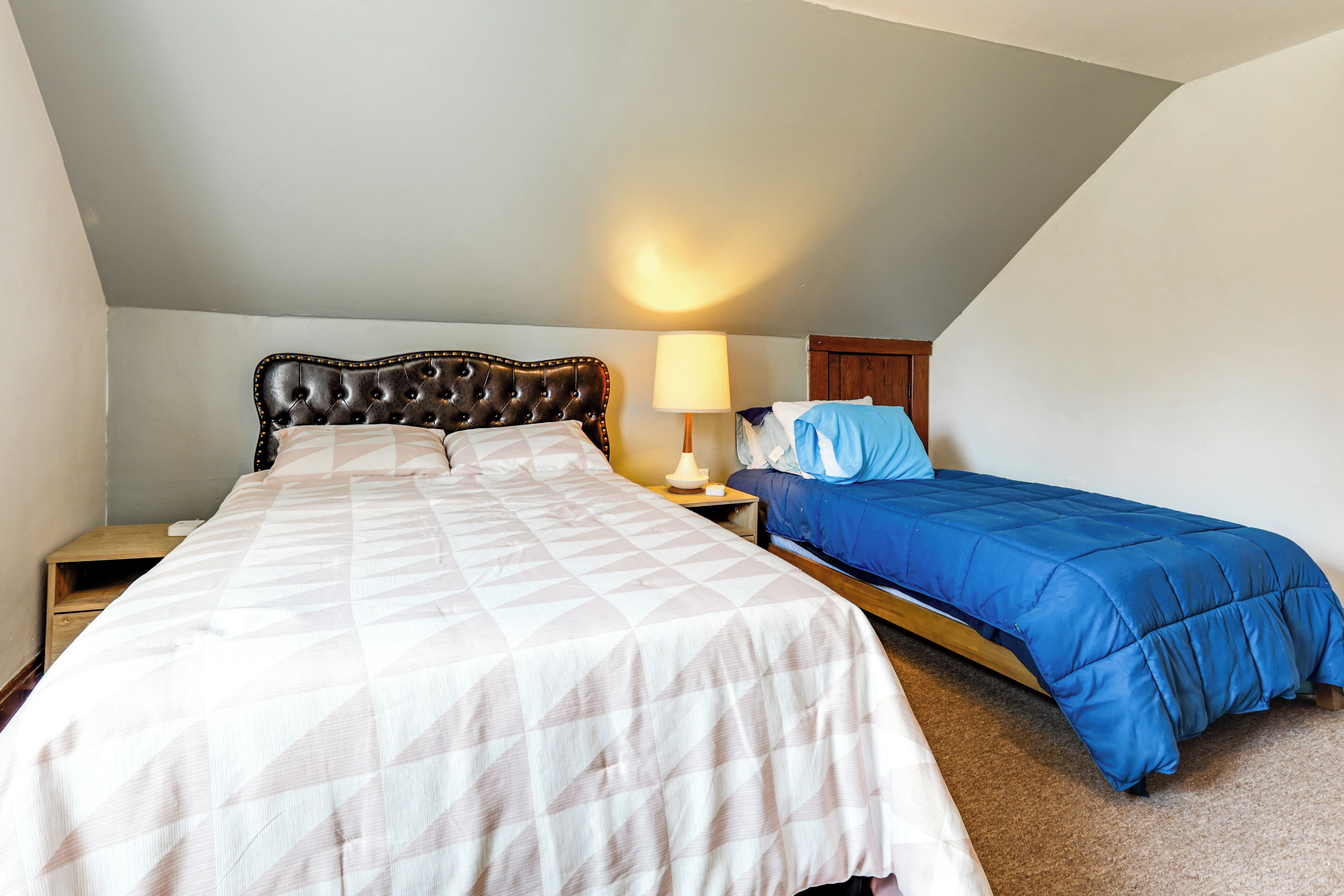 A bedroom with a large bed, a smaller bed, a nightstand, a lamp, and a wooden headboard.