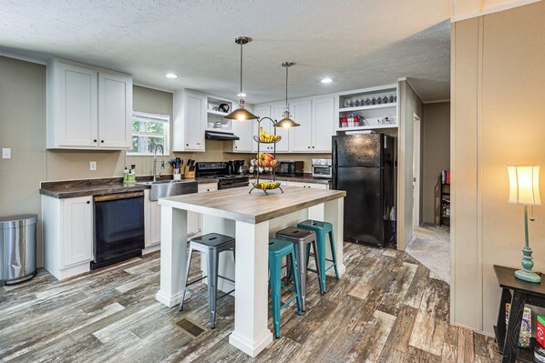 A modern kitchen with white cabinets, a central island with stools, a refrigerator, and a microwave.