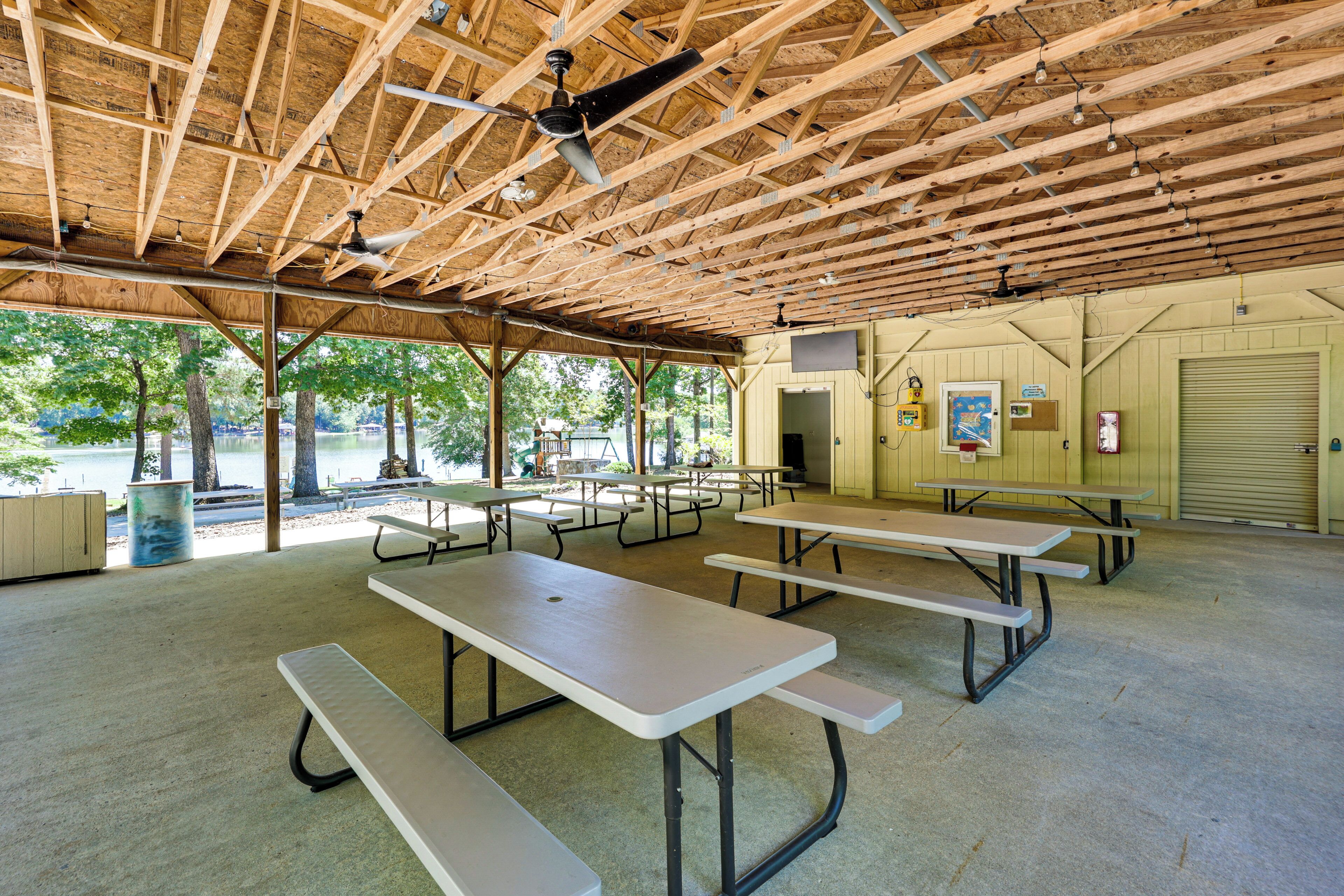 A covered picnic area with multiple picnic tables, ceiling fans, and a view of a lake.