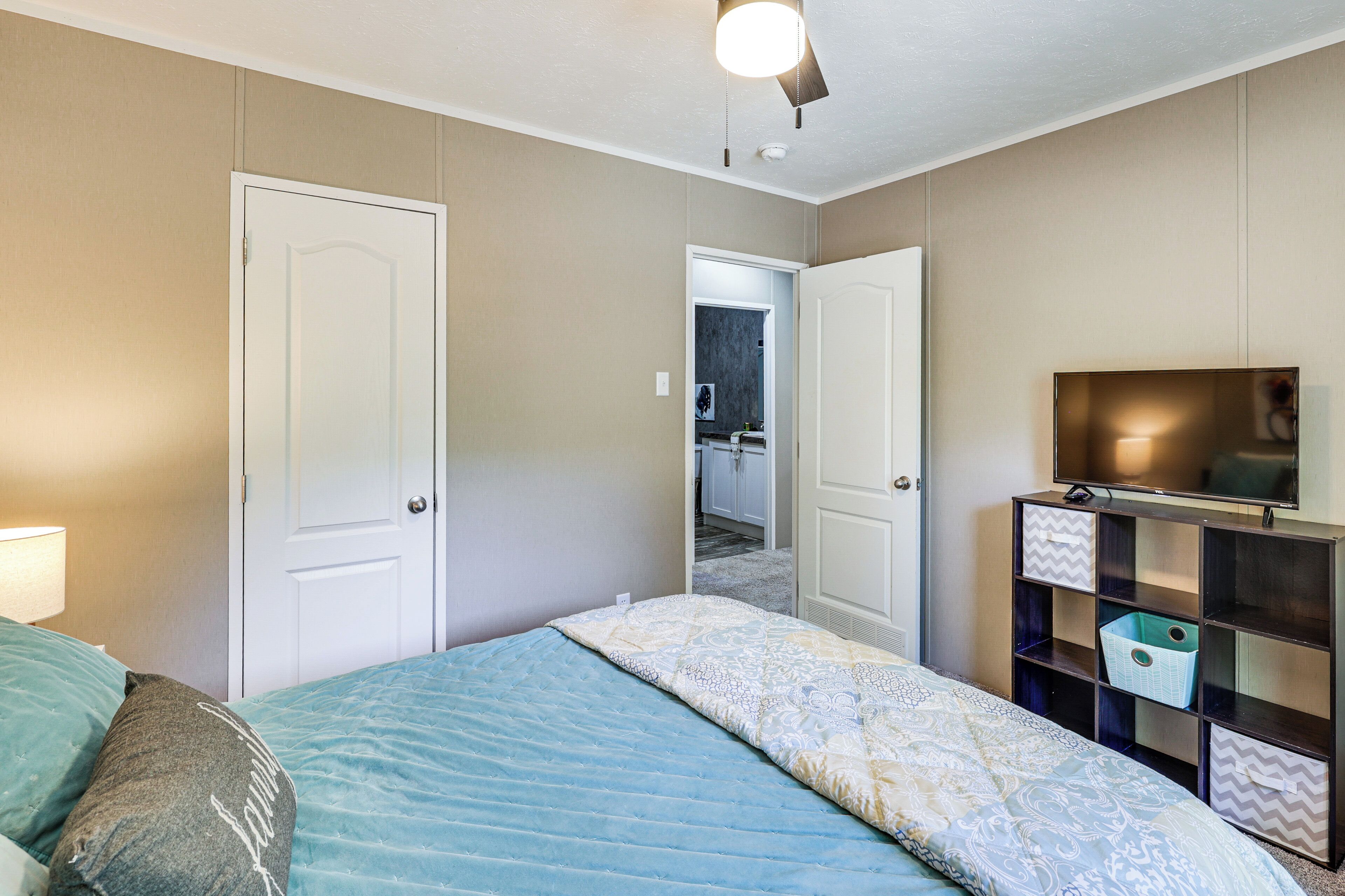 A bedroom with a bed, a TV, a wardrobe, and a door leading to another room.