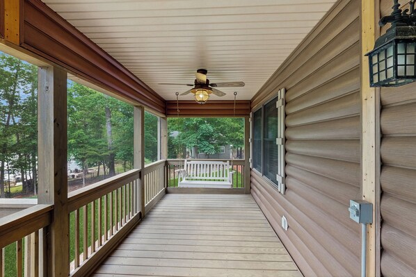 A covered porch with a ceiling fan, wooden railing, and a bench.