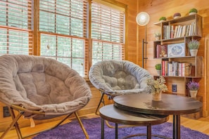 A cozy room with two large, plush chairs, a round table, and a bookshelf filled with books and plants. - Dock & Fire Pit! Lake Gaston Cabin in Macon (Macon)