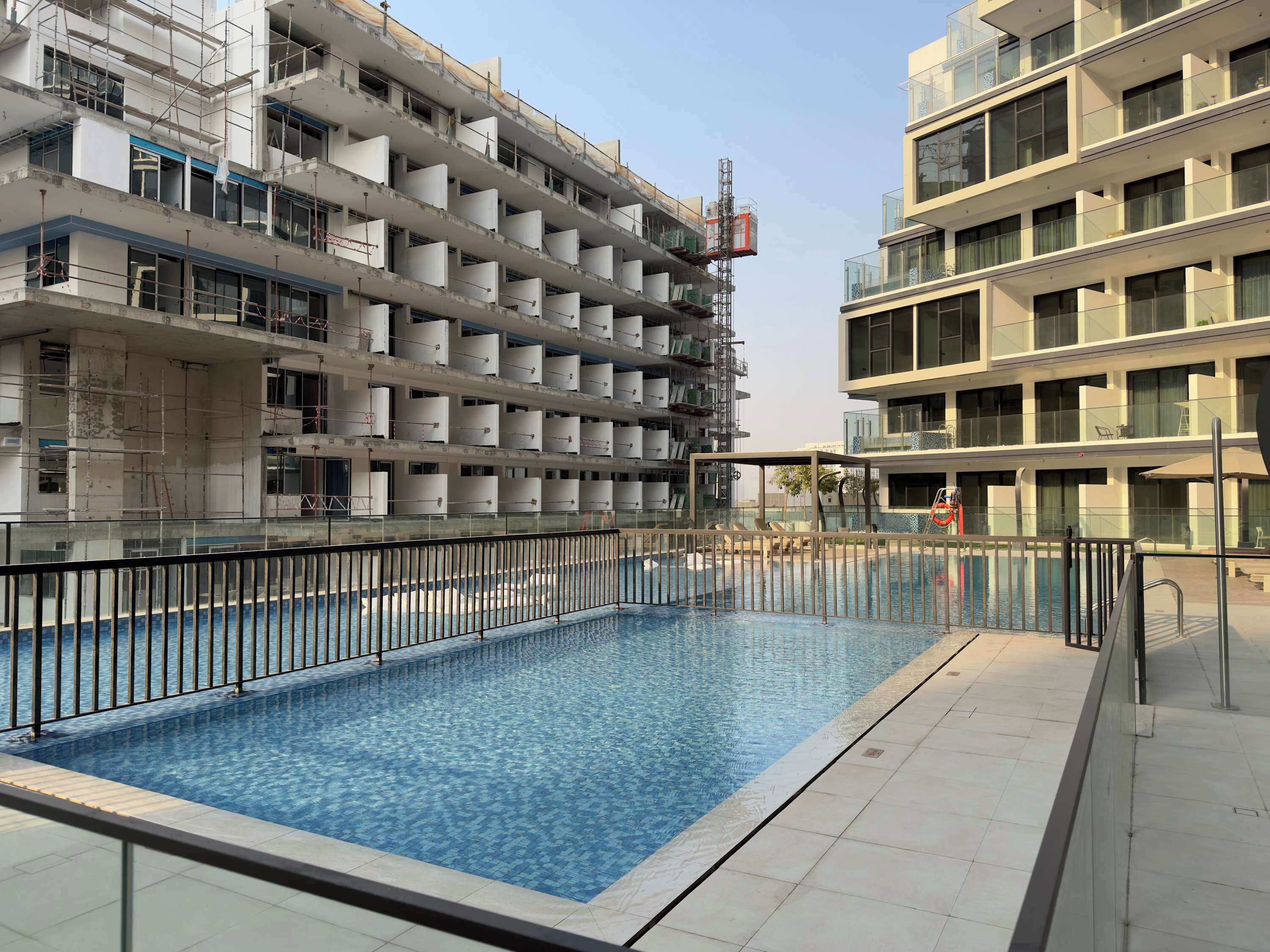 A swimming pool with a tiled deck, surrounded by a metal fence.