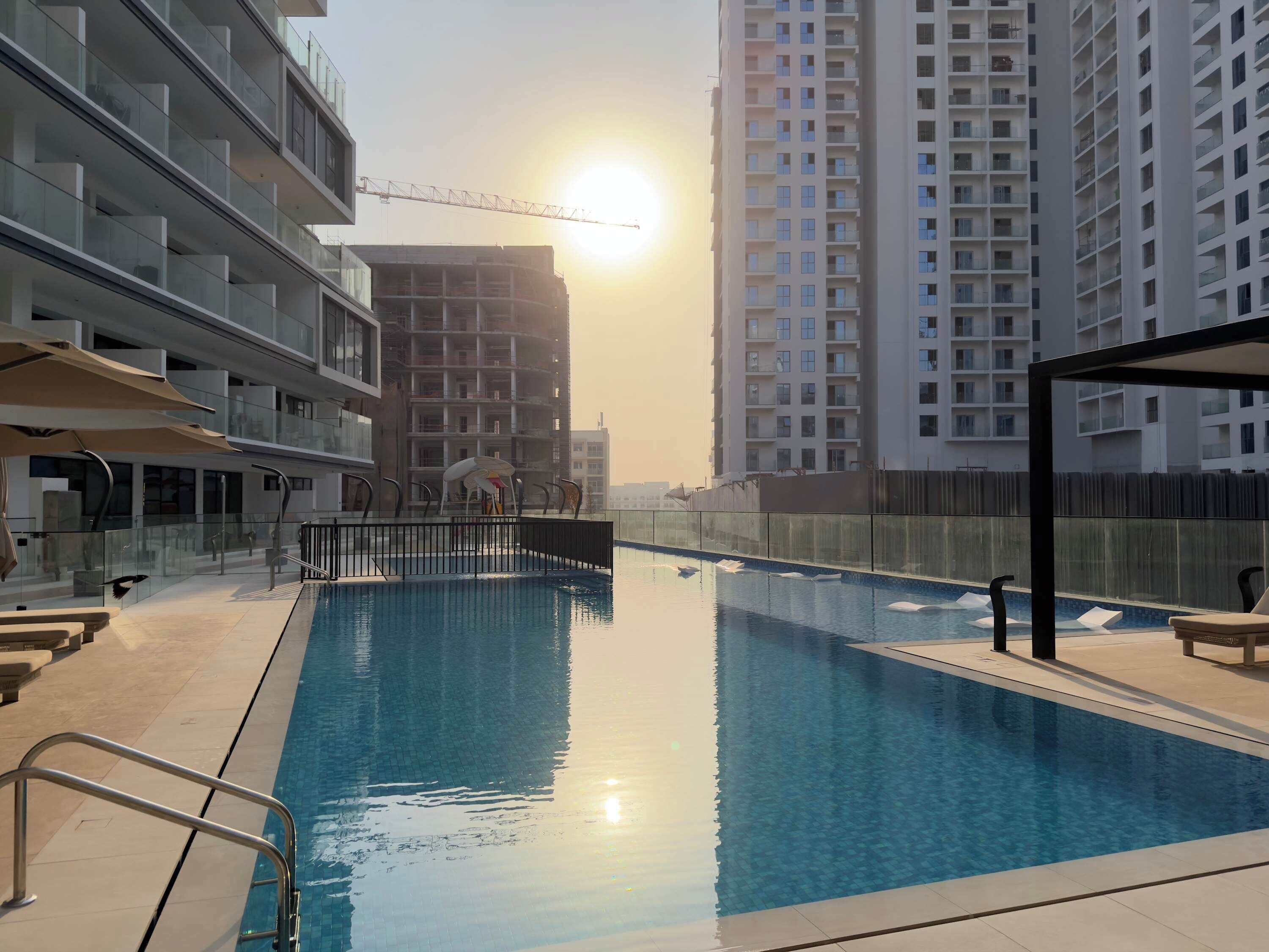 A swimming pool with a sunlit background, surrounded by high-rise buildings.