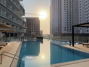 A swimming pool with a sunlit background, surrounded by high-rise buildings. - Arjan Studio with Pool View, Jogging Track & BBQ (Arjan)