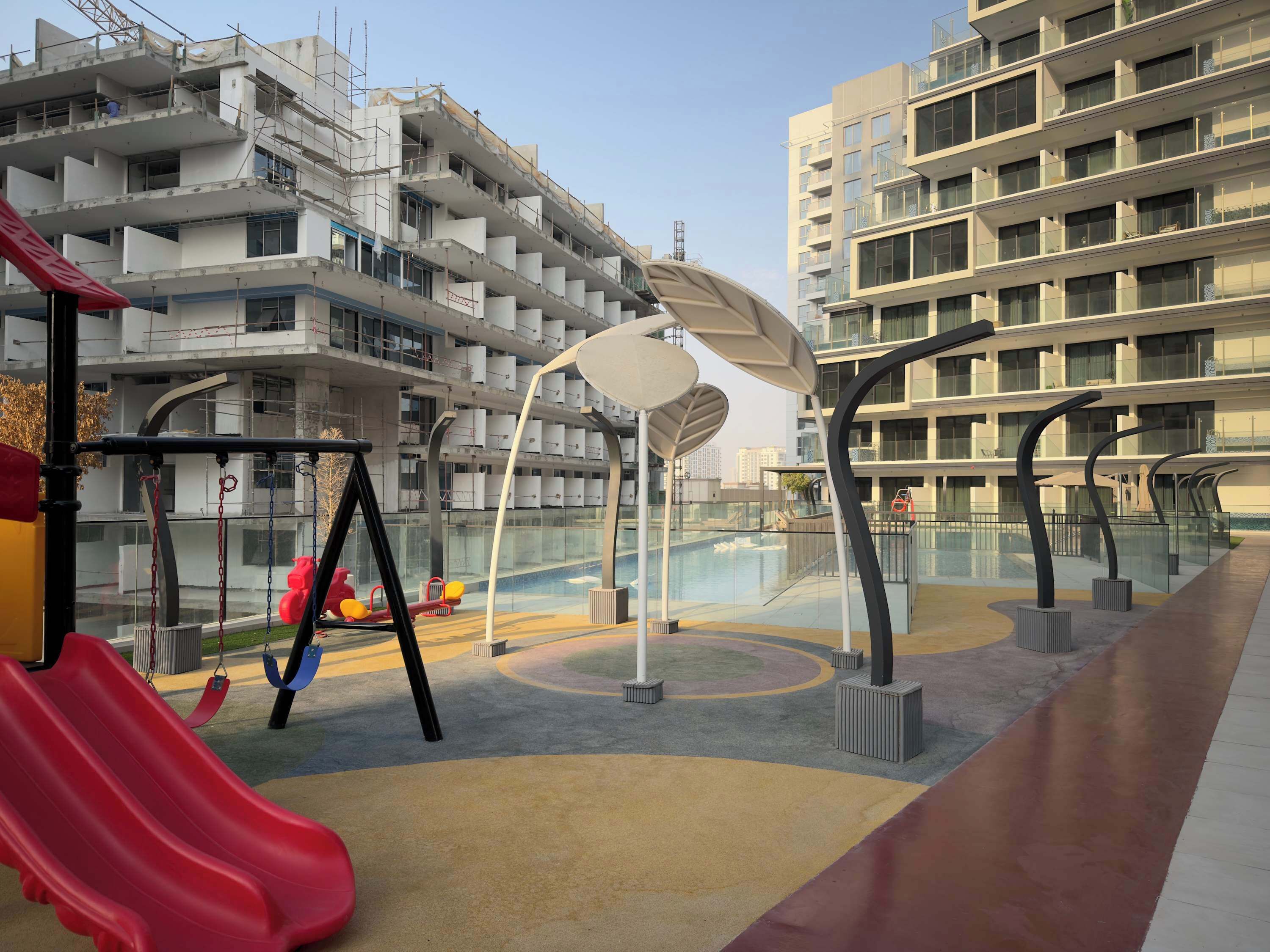 Een speelplaats met glijbanen en schommels, omringd door moderne appartementen.