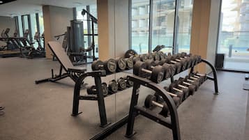A gym with exercise equipment, including dumbbells and benches, and large windows offering a view of the outside.