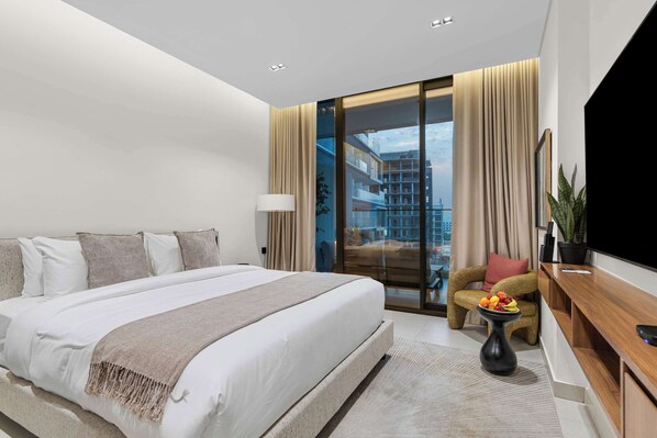 A modern hotel room with a large bed, a TV, a desk, and a view of the cityscape. - Arjan Studio with Pool View, Jogging Track & BBQ (Arjan)