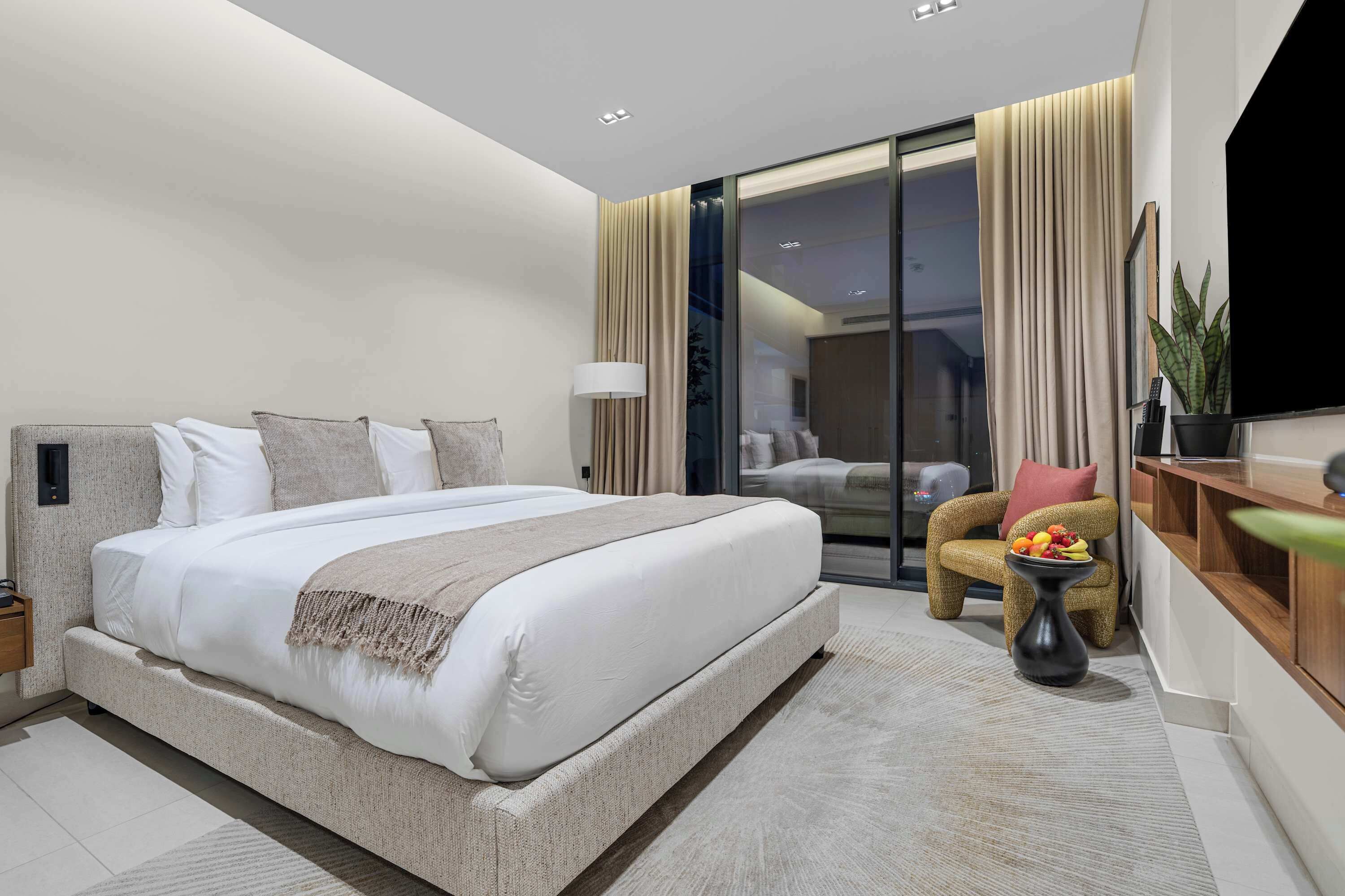 Une chambre d’hôtel moderne avec un grand lit, un coin salon agrémenté d’une plante et une vue sur l’extérieur grâce à une porte vitrée.