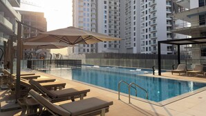A swimming pool with lounge chairs and umbrellas, surrounded by high-rise buildings. - Arjan Studio with Pool View, Jogging Track & BBQ (Arjan)