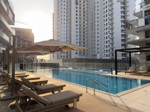 A swimming pool with lounge chairs and umbrellas, surrounded by high-rise buildings. - Arjan Studio with Pool View, Jogging Track & BBQ (Arjan)