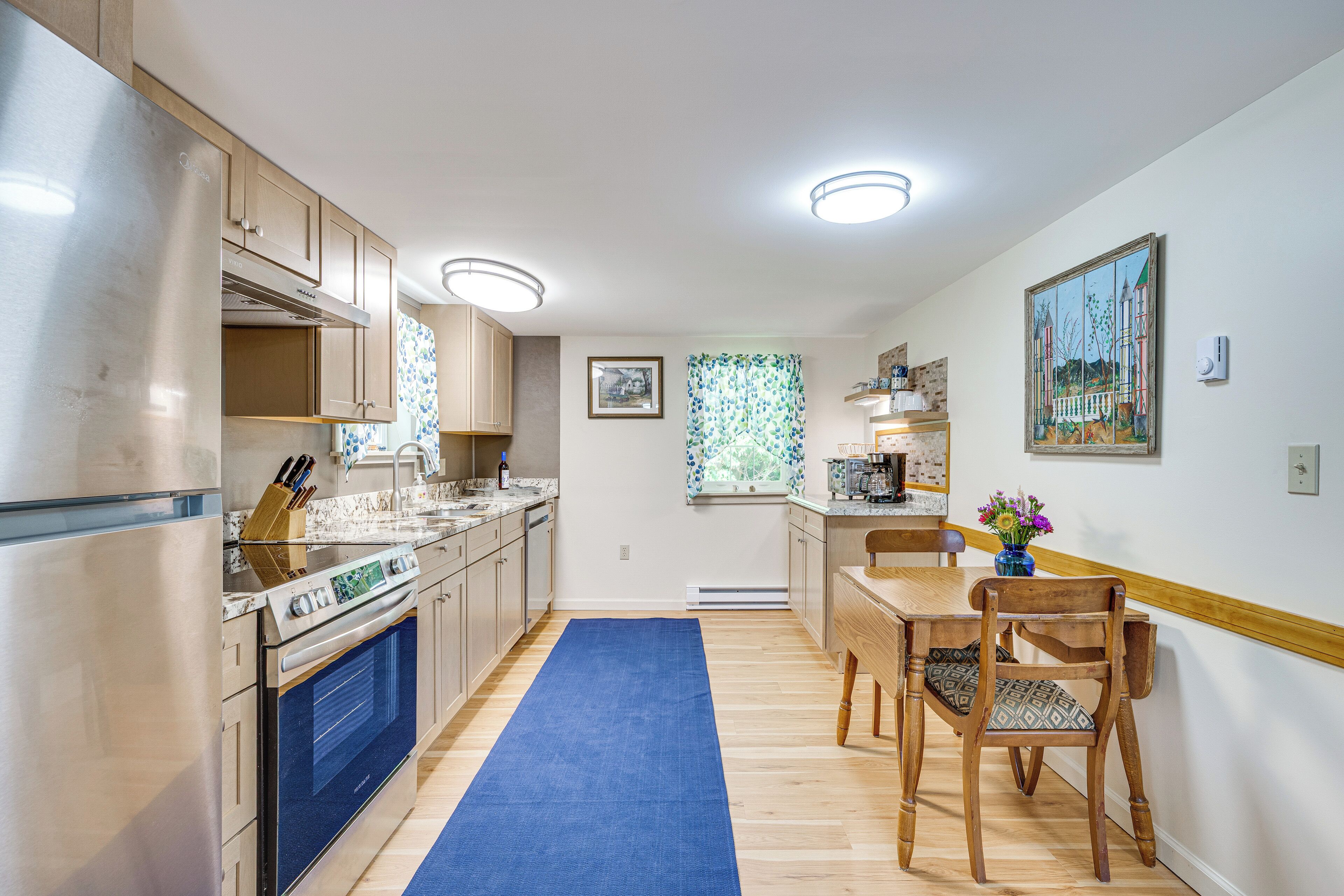 A modern kitchen with a built-in oven, a dining area with a wooden table and chairs, and a window with a view.