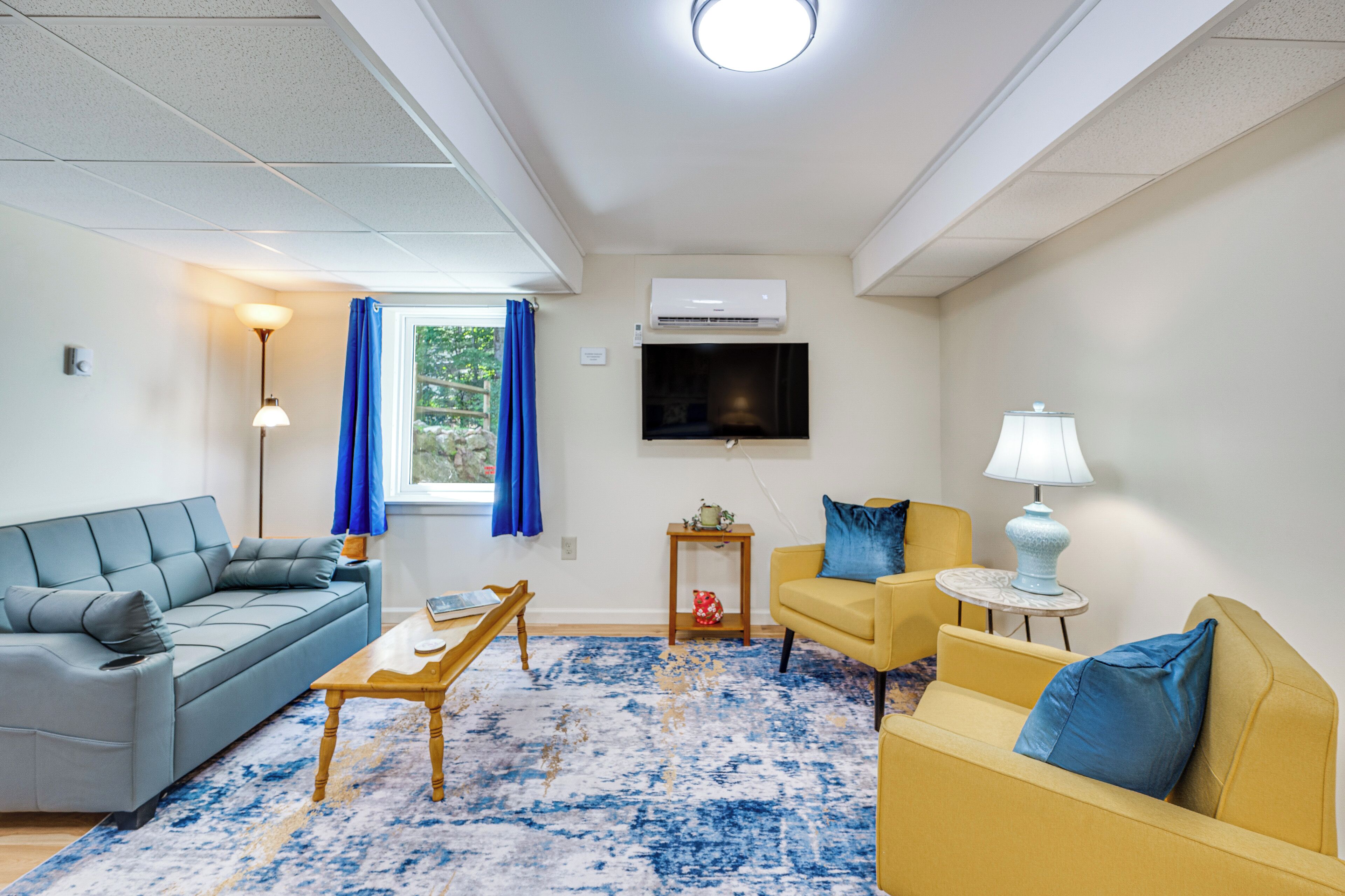 Een woonkamer met een bank, fauteuil, salontafel en een aan de muur bevestigde televisie.