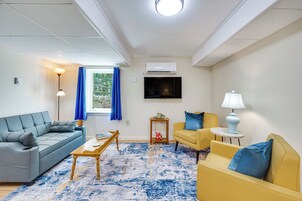 Una sala de estar con un sofá, un sillón, una mesa de centro y un televisor en la pared.