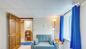A room with a blue sofa, wooden door, bookshelf, and a window with blue curtains. - Ashland Home w/ Deck - Blueberry Overlook (Ashland)