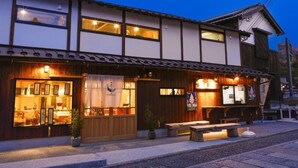 Um edifício japonês tradicional com fachada de madeira, entrada com exposição de objetos e área de estar externa.
