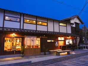 A traditional Japanese building with a wooden exterior, a front entrance with a display of items, and a seating area outside. - Kagoya mizunoto Auberge (Miyazu)