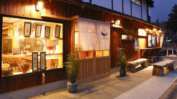 Um edifício tradicional japonês com fachada de madeira, vitrine de vidro e mesas ao ar livre.