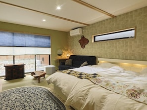 A bedroom with a large bed, a bedside table, a chair, a small table, and a window with blinds. - Kagoya mizunoto Auberge (Miyazu)
