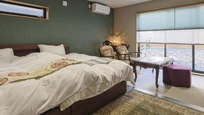 Quarto de hotel com uma cama grande, área de estar com uma mesa e vista para o exterior.