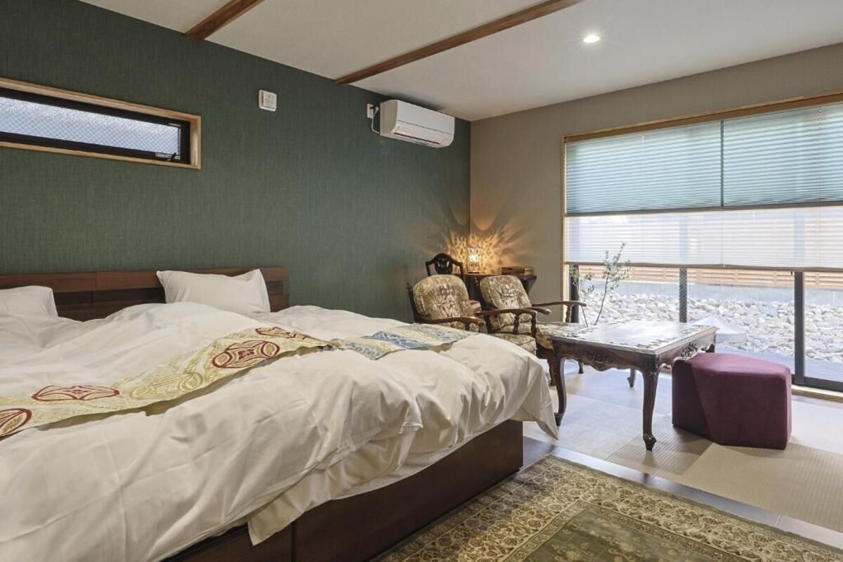 A hotel room with a large bed, a seating area with a table, and a view of the outdoors.