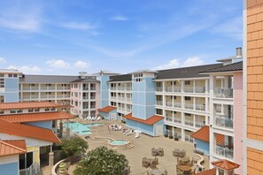 A multi-story hotel with a central courtyard featuring a swimming pool and lounge chairs. - Book Wapacajune Prop 2 | Sandbridge Vacation Rental (virginia beach)