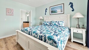 Een slaapkamer met een bed, twee nachtkastjes, een plafondventilator, een deur en een muur met een decoratie van een zeepaard.