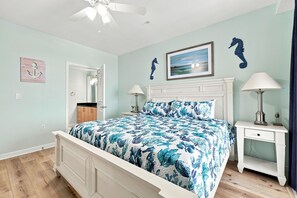 A bedroom with a bed, two bedside tables, a ceiling fan, a door, and a wall with a seahorse decoration. - Book Wapacajune Prop 2 | Sandbridge Vacation Rental (virginia beach)