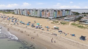 Een strand met een rij kleurrijke, meerverdieping hoge gebouwen, parasols en mensen op het strand.