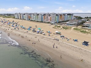 A beach with a row of colorful multi-story buildings, umbrellas, and beachgoers. - Book Wapacajune Prop 2 | Sandbridge Vacation Rental (virginia beach)