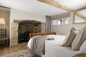 Ein Schlafzimmer mit Kamin aus Stein, einem Bett mit Kissen, einem Holzstuhl und einer Lampe.