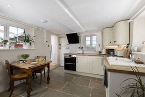 A modern kitchen with white cabinetry, a wooden dining table, and a built-in oven. - Top House -  a country house that sleeps 8 guests  in 4 bedrooms (Shipton-under-Wychwood)