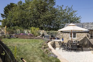 Ein Steinhaus mit Terrasse, Sitzgelegenheit im Freien und einem großen Baum im Hintergrund.