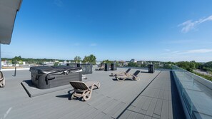 Eine Dachterrasse mit Liegestühlen, einem Grill und einem Glasgeländer mit Blick auf die Stadt.