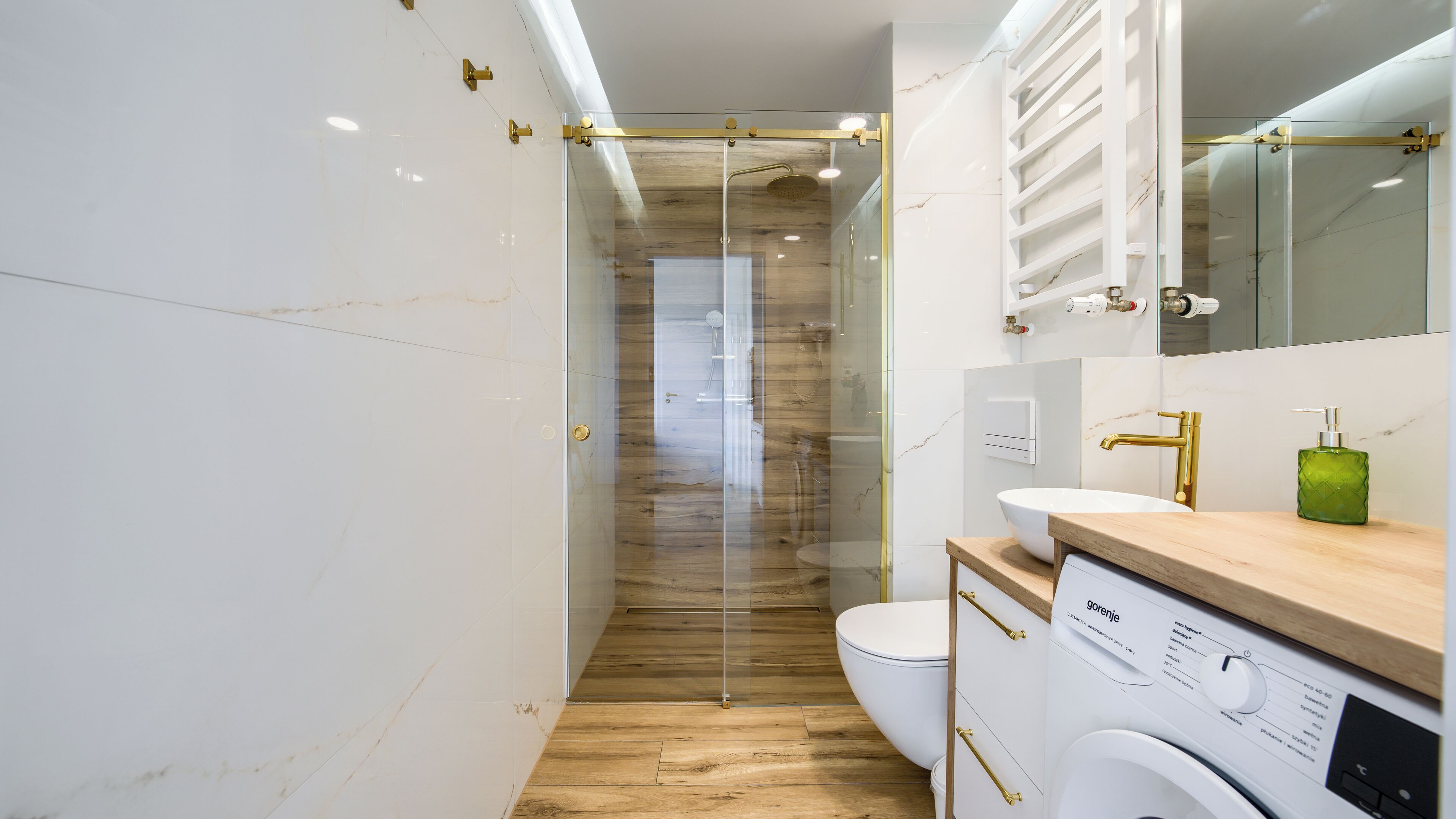 Een moderne badkamer met een douchecabine van glas, een houten wastafelmeubel en een ingebouwde wasmachine.
