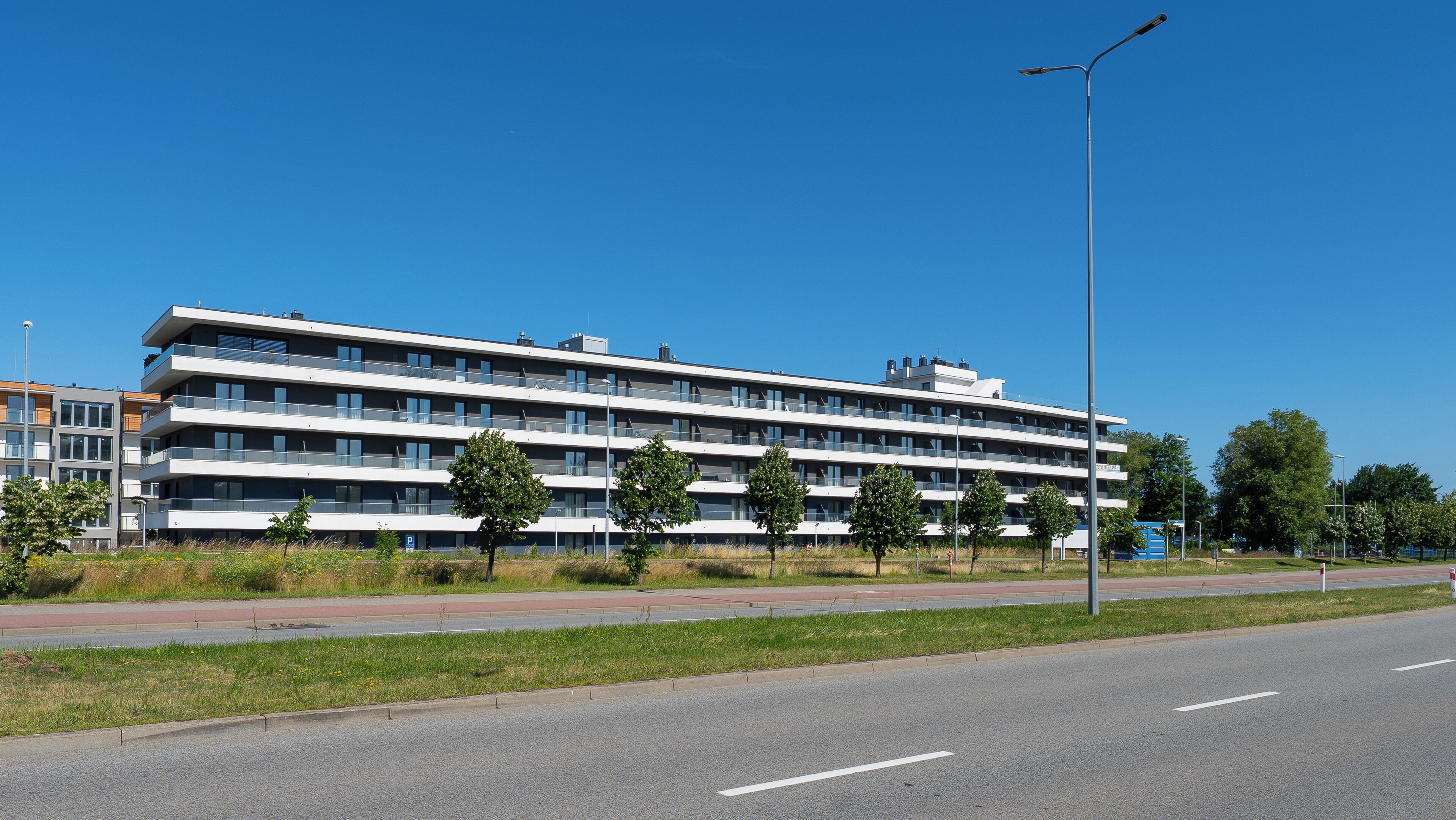 A multi-story hotel with balconies, a parking lot, and a clear blue sky.