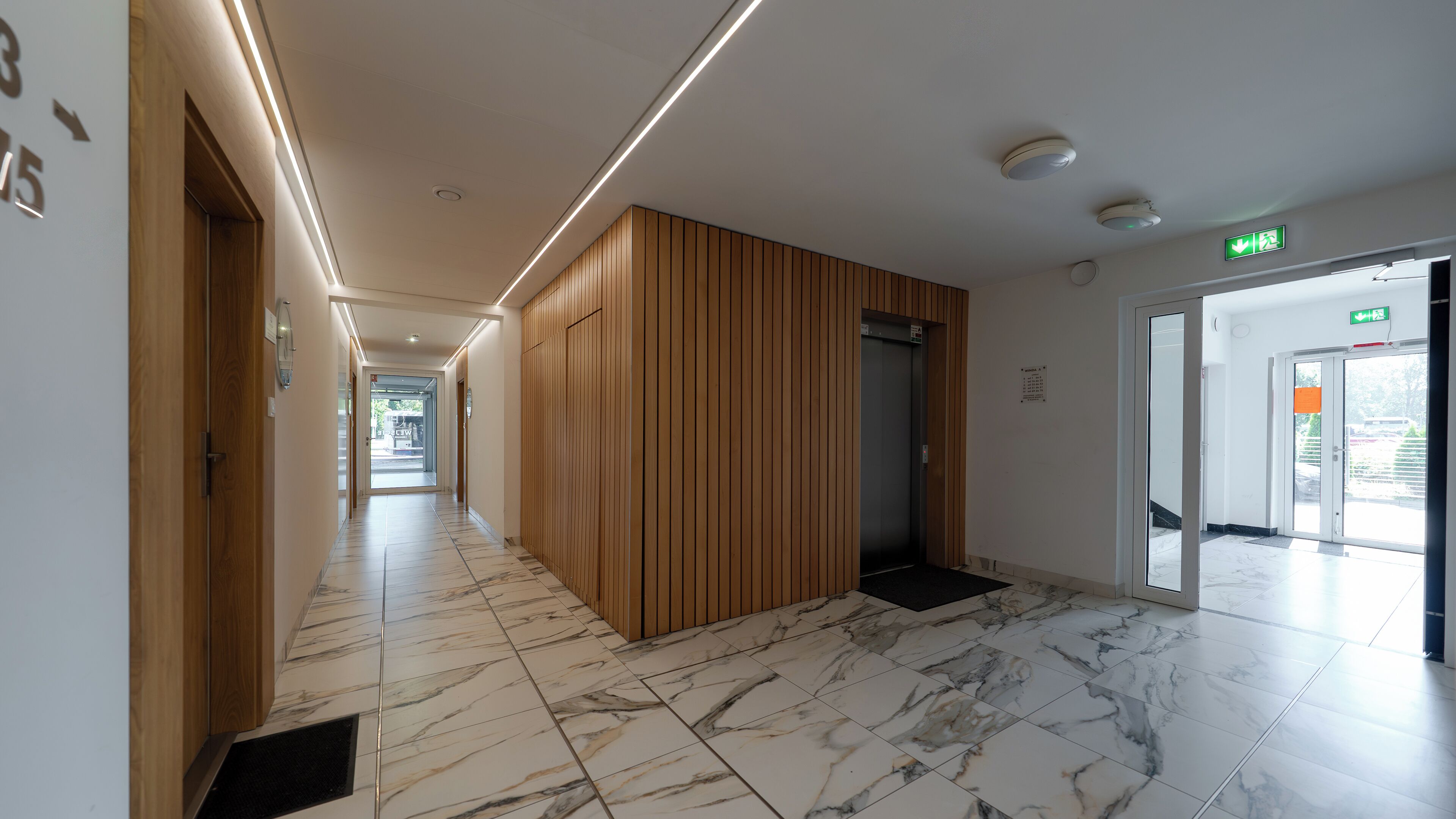 A modern hallway with a marble floor, wooden paneling, and an elevator.