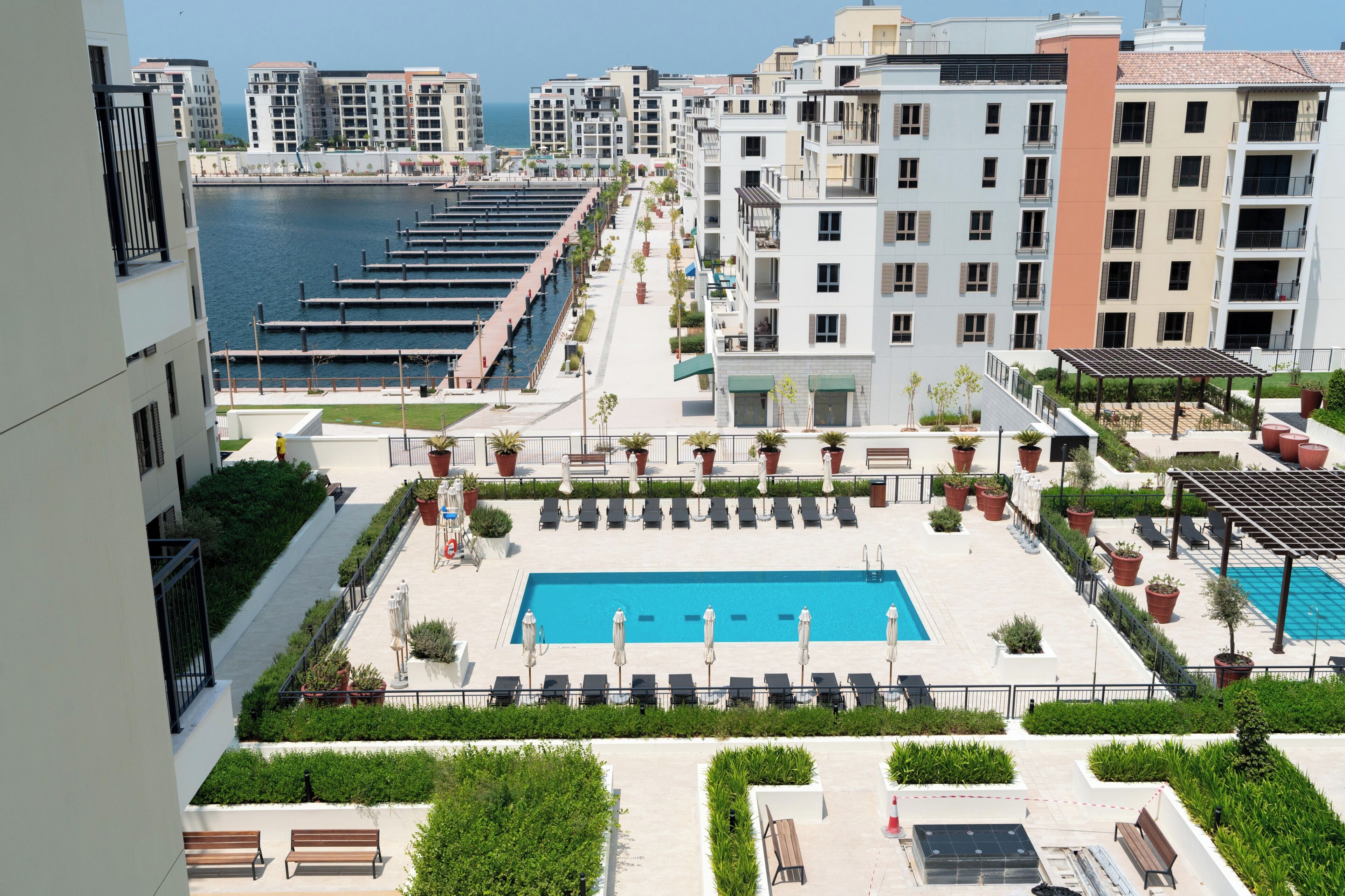 Área de piscina no terraço com vista clara para o mar, rodeada por edifícios modernos e um porto de iates.