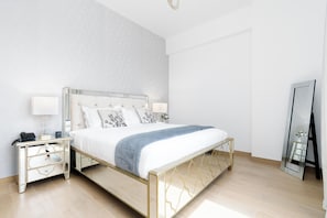 A modern bedroom with a large bed, bedside tables, a mirror, and a nightstand. - bnbme - La Voile 1 - 1BR (Dubai)