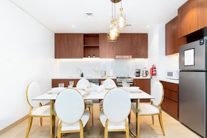 A modern kitchen with a dining table set for six, wooden cabinets, stainless steel appliances, and a pendant light fixture. - bnbme - La Voile 1 - 1BR (Dubai)