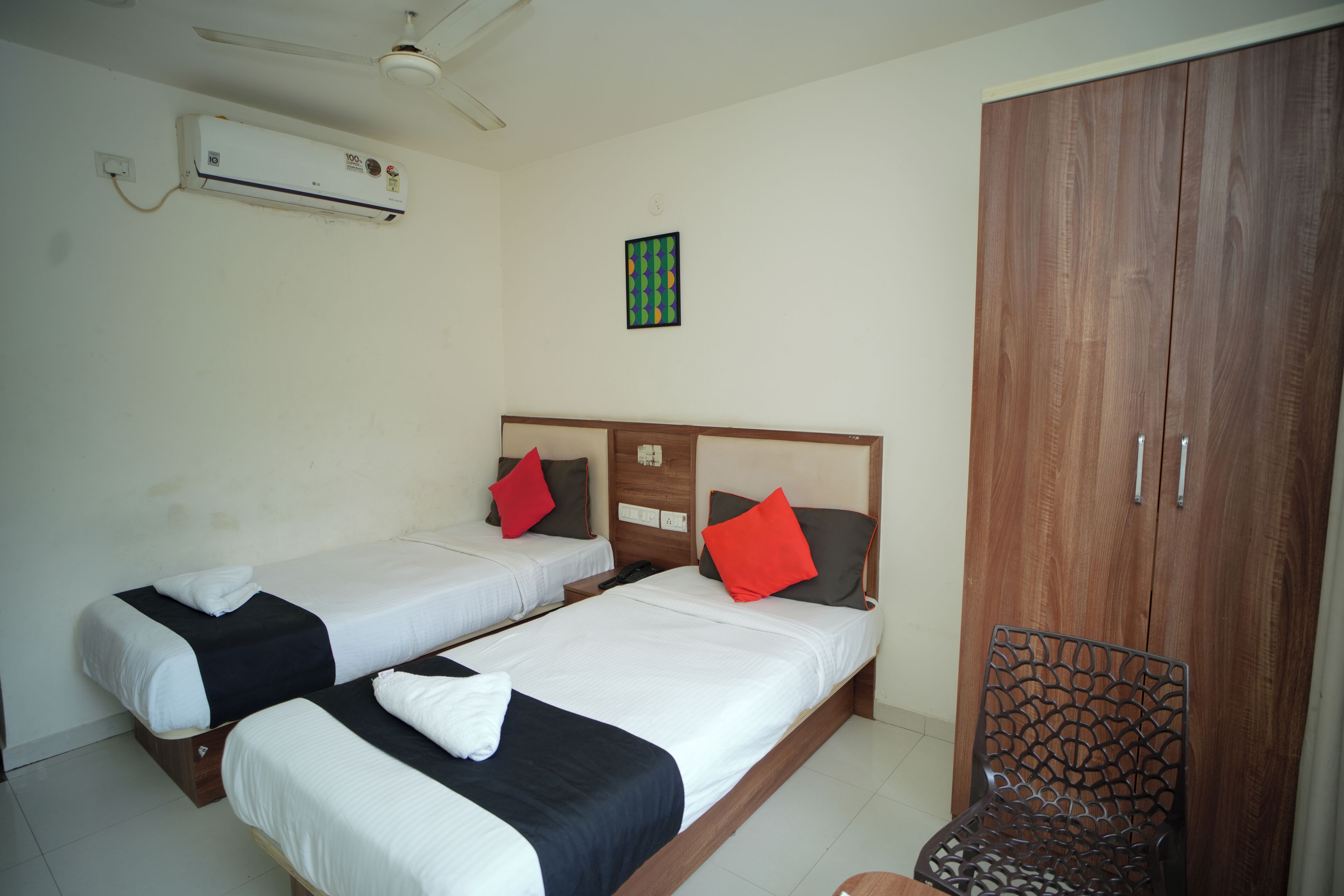 A hotel room with two single beds, a wardrobe, an air conditioning unit, and a small table.