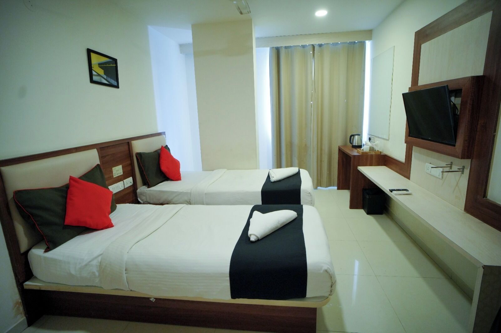 Habitación de hotel con dos camas, un escritorio, un televisor y una ventana con cortinas.