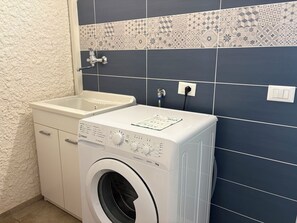 Ein Waschbereich mit Waschmaschine, Spüle und einer gefliesten Spritzwand.