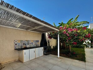 Ein Außenbereich mit Küche, einer gefliesten Spritzwand, einem Grill und einer Pergola.