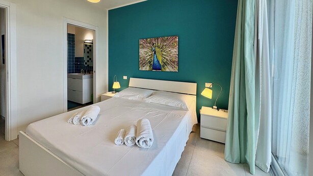 Ein Hotelzimmer mit einem Bett, zwei Nachttischlampen, einem Bild an der Wand und einem Fenster mit Vorhängen.