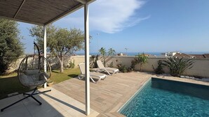 Ein Poolbereich mit einer Hängematte, Liegestühlen und Blick auf das Meer.