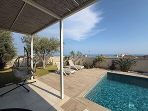 Ein Poolbereich mit einer Hängematte, Liegestühlen und Blick auf das Meer.